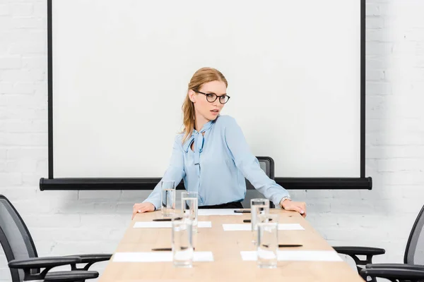 Attractive young businesswoman sitting alone at conference hall and looking away — Stock Photo