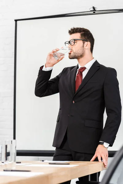 Atraente jovem empresário água potável no escritório moderno — Fotografia de Stock