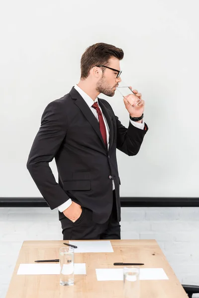 Schöner junger Geschäftsmann trinkt Wasser in modernem Büro — Stockfoto