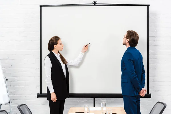 Businesswoman making presentation and pointing at blank whiteboard at modern office — Stock Photo