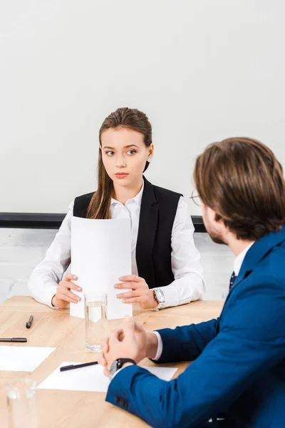 Attractive young businesswoman listening to colleague while holding documents at modern office — Stock Photo