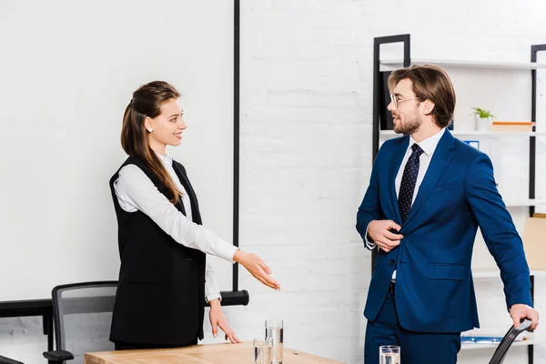 Selbstbewusste junge Geschäftsfrau zeigt ihrem Partner im Konferenzraum, wo er Platz nehmen soll — Stockfoto