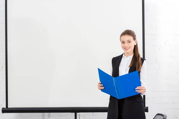 Attraktive junge Geschäftsfrau mit Mappe vor leerem Whiteboard im modernen Büro — Stockfoto