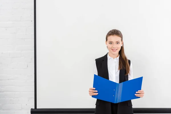 Hermosa joven empresaria con carpeta delante de pizarra blanca en blanco en la oficina moderna - foto de stock