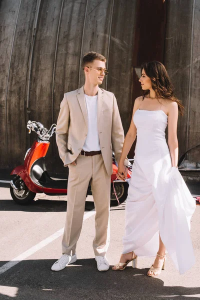 Schönes Hochzeitspaar hält Händchen gegen Motorroller in der Stadt — Stockfoto