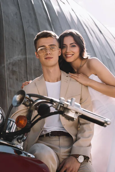 Casamento sorridente casal abraçando e sentado em scooter retro — Fotografia de Stock