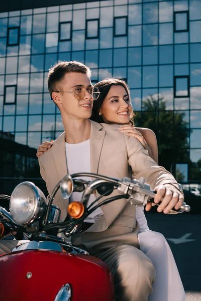 Feliz boda pareja sentado en la vendimia scooter contra edificio en la ciudad - foto de stock