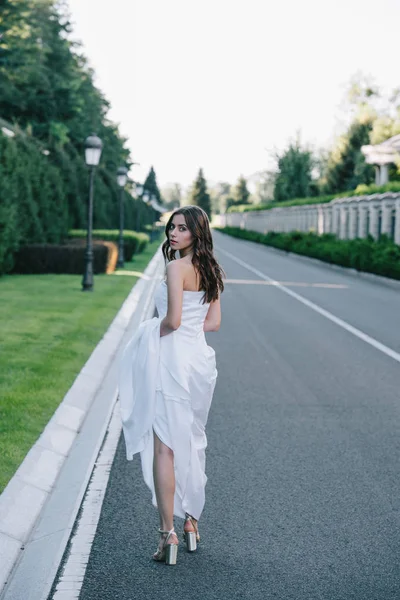 Back view of beautiful bride in wedding dress walking on road — Stock Photo