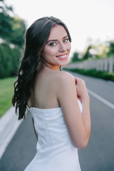 Noiva sorridente em vestido de noiva tradicional posando na estrada — Fotografia de Stock