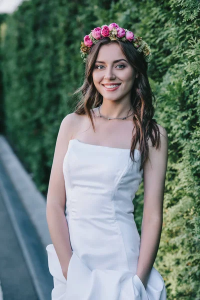Niña sonriente posando en vestido de novia blanco tradicional y corona floral - foto de stock