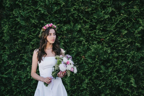 Bella sposa in posa in abito bianco tradizionale con corona e bouquet da sposa — Foto stock