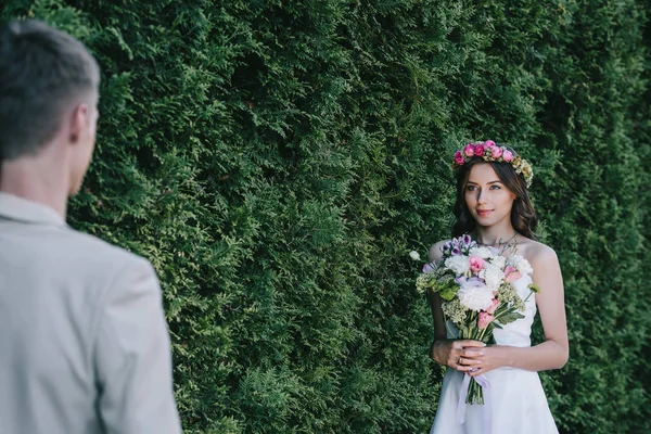 Selektiver Fokus der schönen Braut im Kranz mit Brautstrauß auf den Bräutigam — Stockfoto