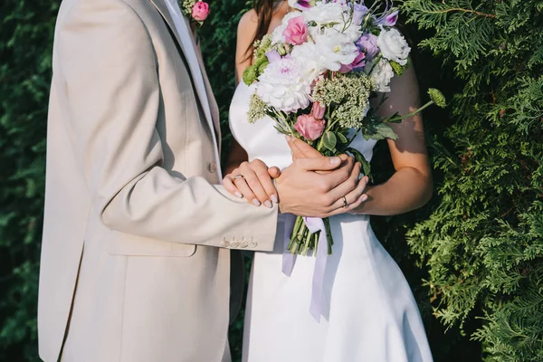 Partial view of elegant wedding couple holding flower bouquet — Stock Photo