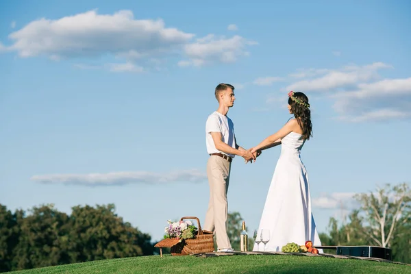 Beau couple de mariage tenant la main sur la pelouse avec pique-nique romantique — Photo de stock