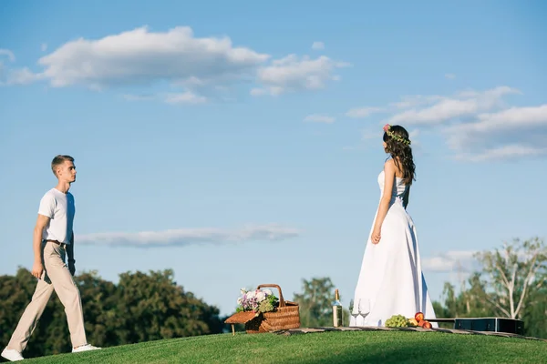 Groom going to bride in white wedding dress on picnic — Stock Photo