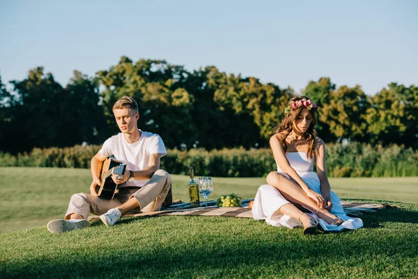 Groom playing guitar for upset bride during romantic picnic on lawn — Stock Photo