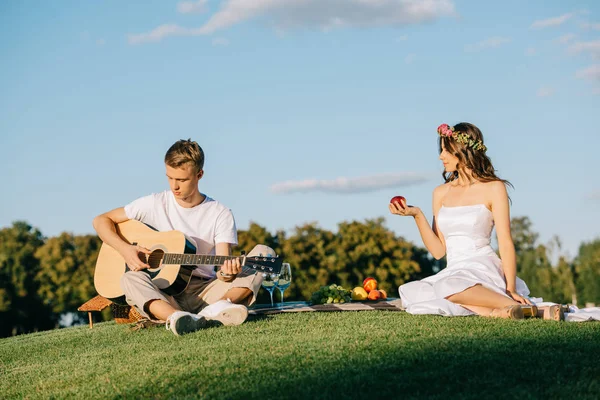 Noivo tocando na guitarra acústica para noiva durante piquenique romântico — Fotografia de Stock