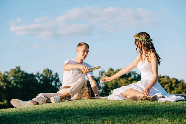 Groom pouring wine into glass for bride on picnic — Stock Photo