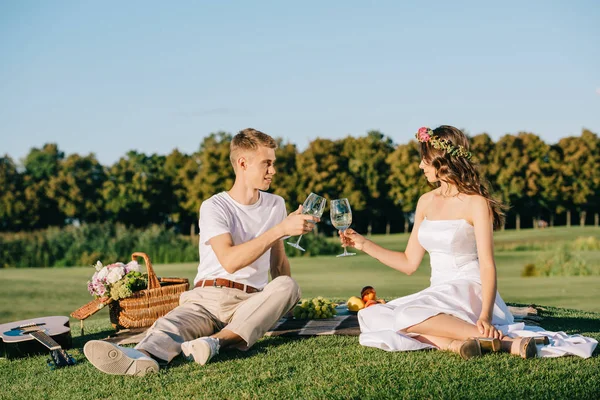 Happy wedding couple clinking with glasses of wine during picnic on green lawn — Stock Photo