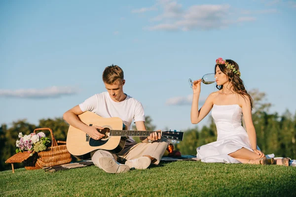 Наречений грає на акустичній гітарі, а наречена п'є вино на романтичному пікніку — стокове фото