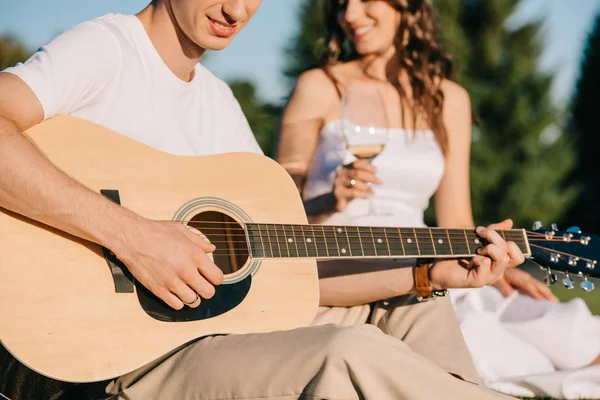 Novio tocando en la guitarra acústica para novia con copa de vino - foto de stock