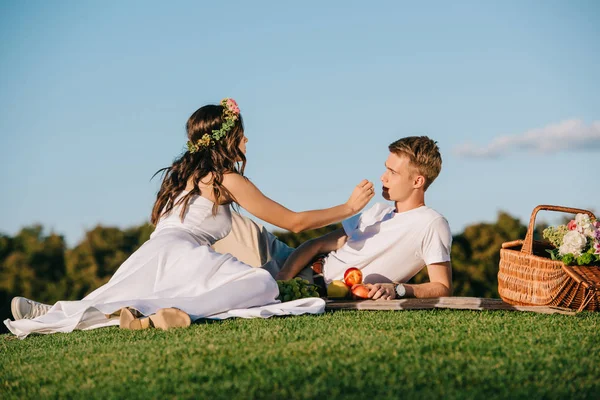 Happy wedding couple resting on picnic with fruits in wicker basket — Stock Photo