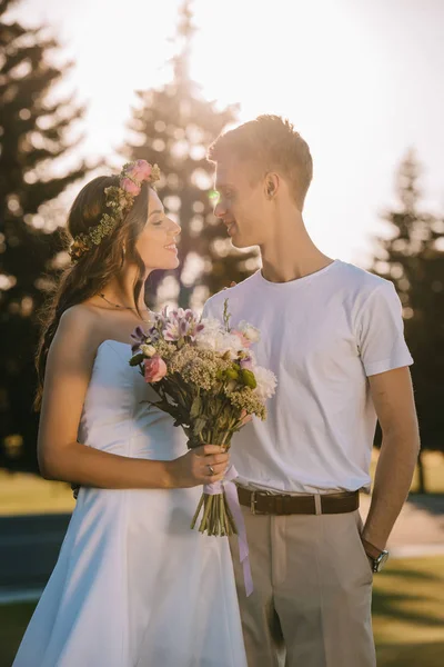 Elegant wedding couple with bouquet smiling to each other — Stock Photo