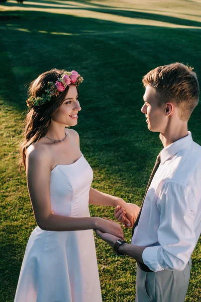 Vue grand angle de beau jeune couple de mariage tenant la main et se souriant mutuellement dans le parc — Photo de stock