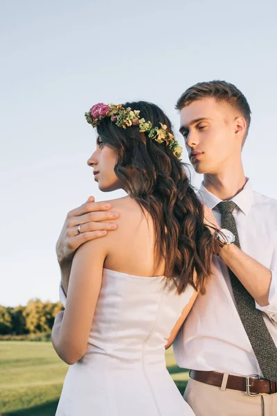 Young groom embracing beautiful young bride in park — Stock Photo