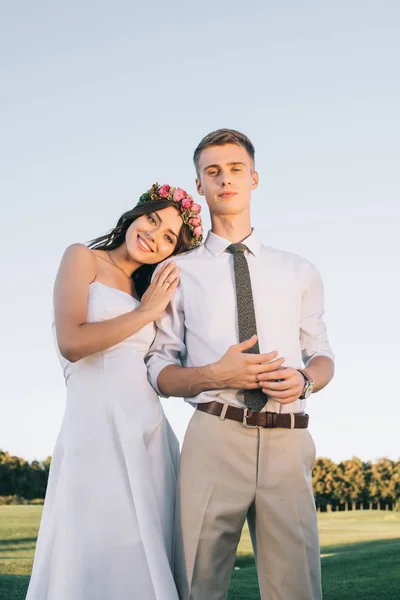 Bajo ángulo vista de hermosa joven pareja de boda de pie juntos y sonriendo a la cámara en el parque - foto de stock