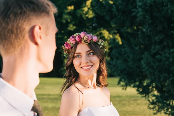 Schnappschuss der schönen glücklichen jungen Braut und des Bräutigams, die einander im Park lächeln — Stockfoto