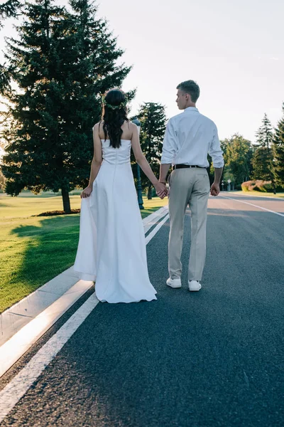 Vue arrière du jeune couple de mariage tenant la main et marchant sur la passerelle dans le parc — Photo de stock