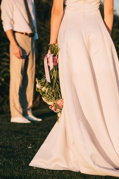 Cropped shot of young bride in beautiful dress holding wedding bouquet — Stock Photo