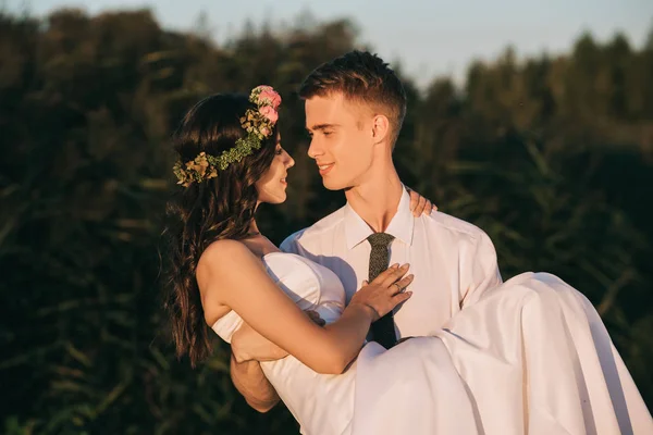 Heureux jeune marié portant belle mariée tendre dans le parc — Photo de stock