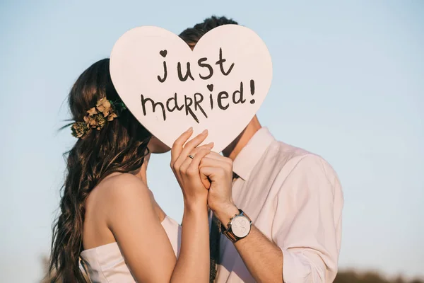 Junges Hochzeitspaar küsst und hält Herz mit frisch verheirateter Inschrift — Stockfoto