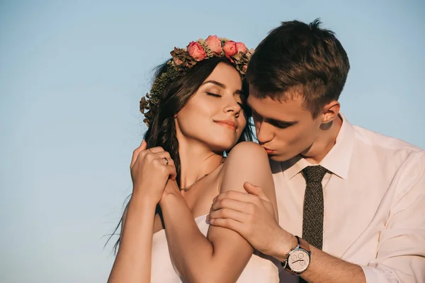 Young groom kissing beautiful smiling bride against blue sky — Stock Photo