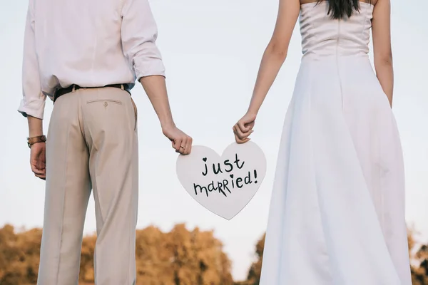 Tiro recortado de jovem casal de casamento segurando coração com inscrição recém-casada — Fotografia de Stock