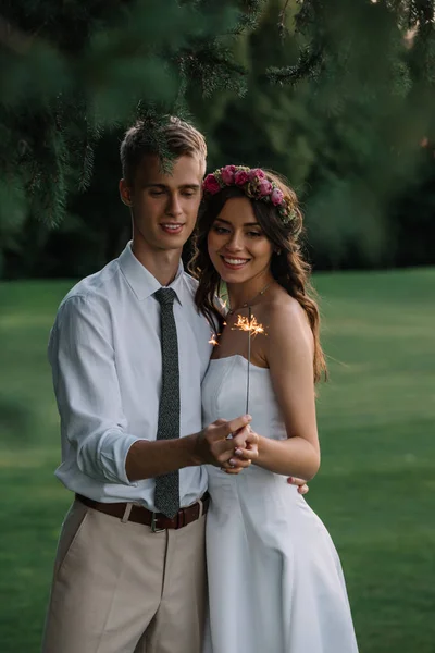 Красивая улыбающаяся молодая романтическая свадебная пара, держащая искру на открытом воздухе — стоковое фото