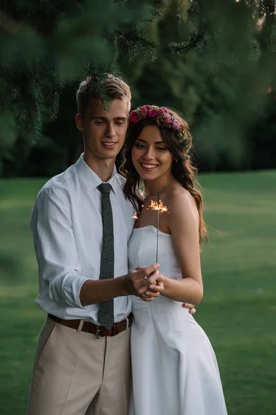 Beautiful smiling young romantic wedding couple holding sparkler outdoors — Stock Photo