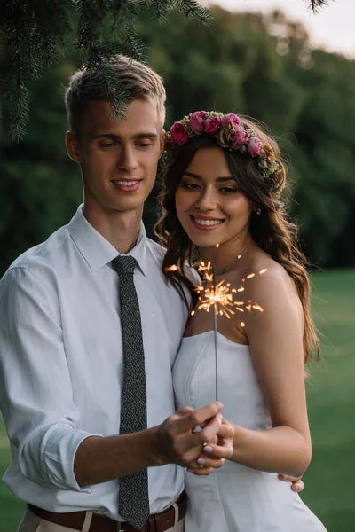 Beautiful happy young romantic wedding couple holding sparkler outdoors — Stock Photo