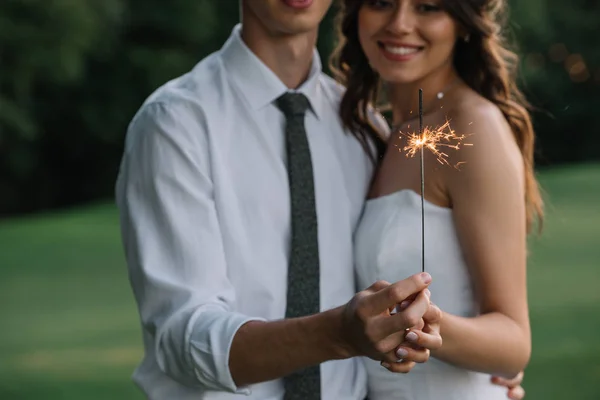 Cropped shot of smiling young wedding couple holding sparkler — Stock Photo