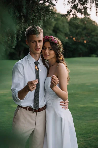 Elegante romántico joven boda pareja celebración de chispas y sonriendo a la cámara - foto de stock