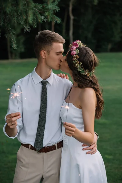 Elegant romantic young wedding couple kissing and holding sparklers outdoors — Stock Photo