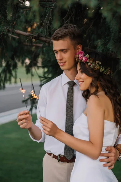 Beautiful happy young wedding couple embracing and holding sparklers — Stock Photo