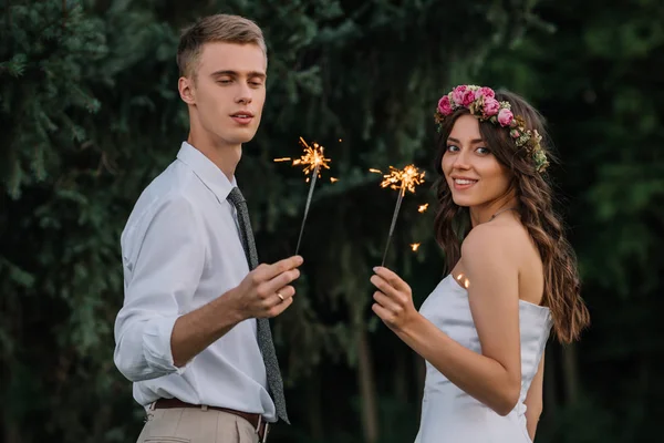 Happy young wedding couple holding sparklers and smiling at camera — Stock Photo