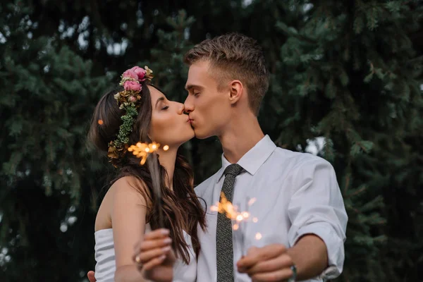 Красивая счастливая молодая свадебная пара целуется и держит искры — стоковое фото