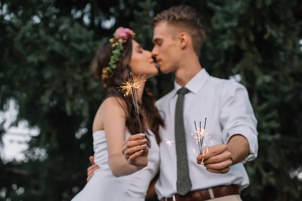 Beautiful young wedding couple kissing and holding sparklers — Stock Photo