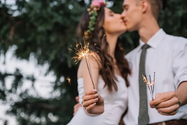 Vue rapprochée du couple heureux de mariage tenant étincelles et baisers, mise au point sélective — Photo de stock