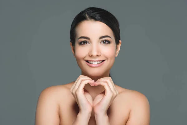 Retrato de bela mulher sorridente com dentes brancos mostrando sinal de coração com as mãos isoladas em cinza — Fotografia de Stock