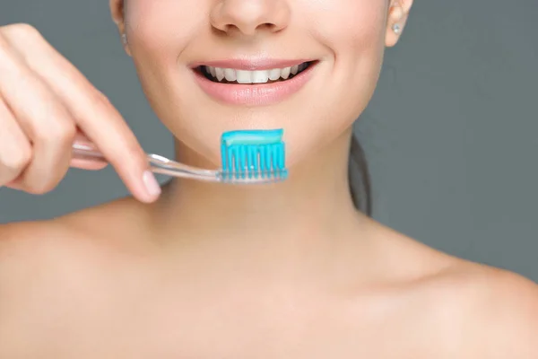 Cropped shot of smiling woman holding tooth brush with tooth paste isolated on grey — Stock Photo